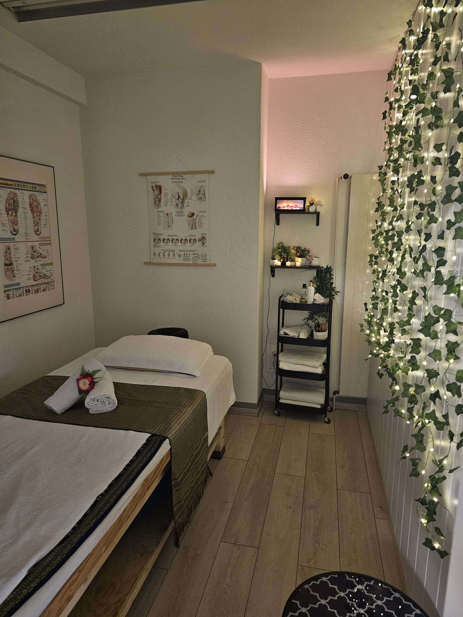 Behandlungsraum mit Fussreflexzonen-Poster, Thai-Massagebett und Efeu-Lichtervorhang