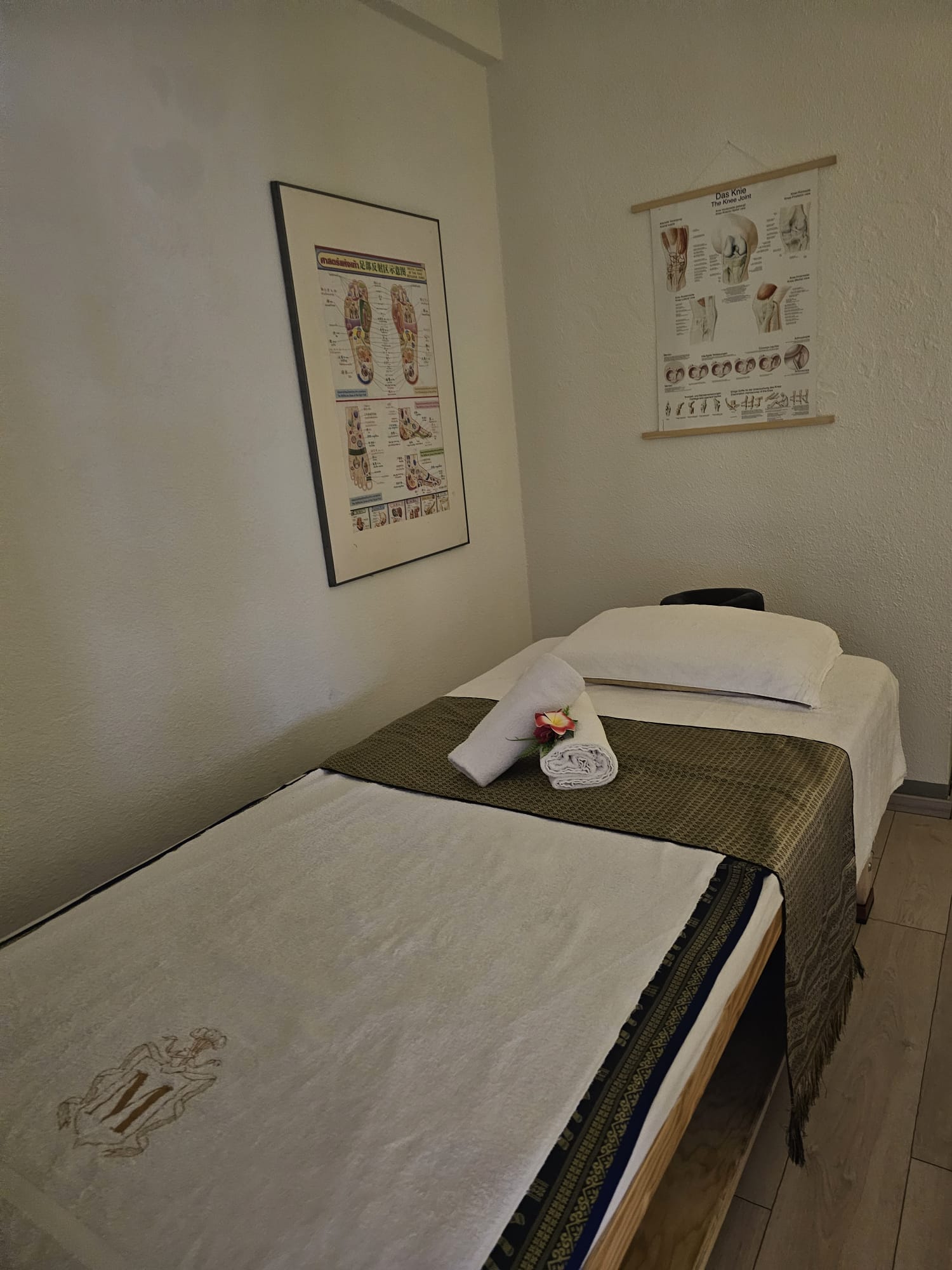 Massagebett mit gerolltem Handtuch, Frangipani-Blüte und Anatomie-Postern