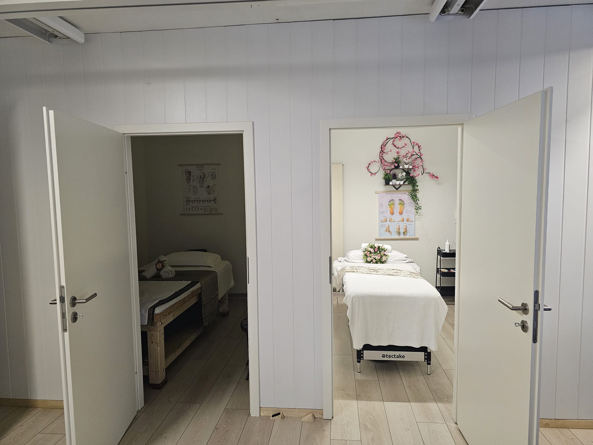 Blick durch zwei geöffnete Türen in die Behandlungsräume mit Massagebetten und Blumendekoration